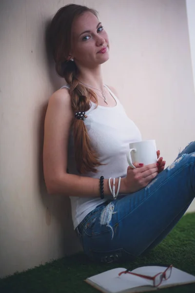 Hermosa mujer sentada en el suelo y sosteniendo una taza. Hermosa mujer — Foto de Stock