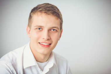Gri arka plan üzerinde oturan gülümseyen genç adam portresi. Genç adam portresi