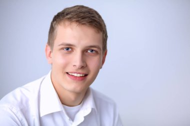 Gri arka plan üzerinde oturan gülümseyen genç adam portresi. Genç adam portresi