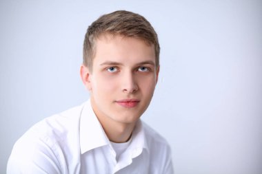 Gri arka plan üzerinde oturan gülümseyen genç adam portresi. Genç adam portresi
