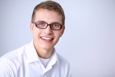 Gri arka plan üzerinde oturan gülümseyen genç adam portresi. Genç adam portresi