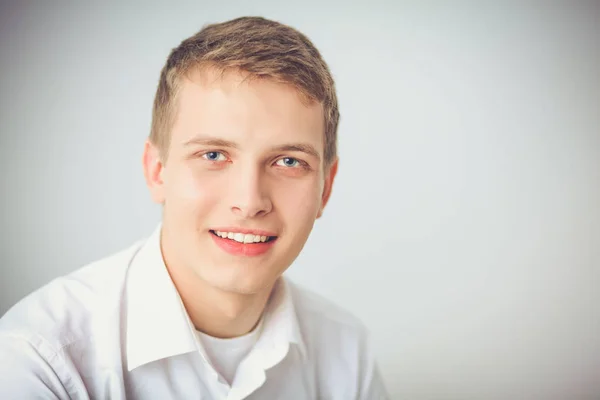 Portré, fiatal férfi mosolyogva ül a szürke háttér. Fiatal férfi portréja — Stock Fotó