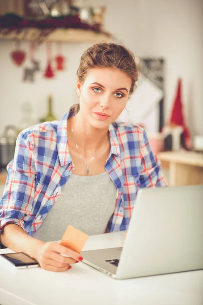 Mujer sonriente compras en línea utilizando la computadora y la tarjeta de crédito en la cocina. Mujer sonriente —  Fotos de Stock