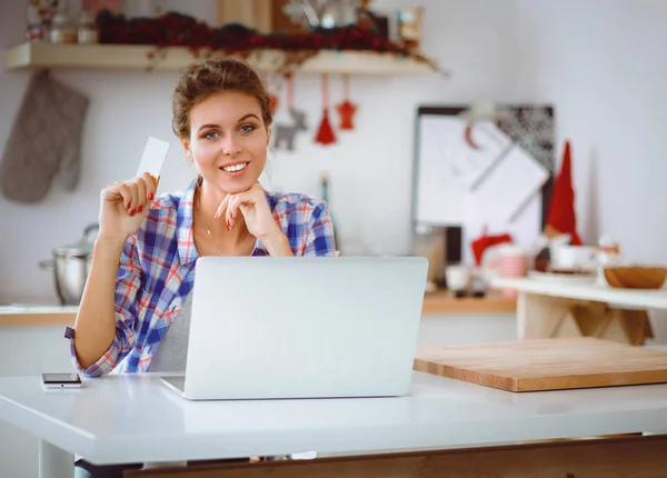 Lachende vrouw online winkelen met behulp van computer- en credit card in keuken. Lachende vrouw — Stockfoto