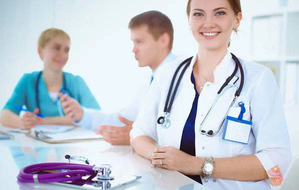 Bonito jovem sorridente médico feminino sentado na mesa — Fotografia de Stock