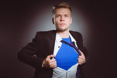 Genç işadamı hareket ve bir süper kahraman gibi gömleğini, yırtılma gri arka plan üzerinde izole. Genç işadamı