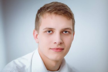 Gri arka plan üzerinde oturan gülümseyen genç adam portresi. Genç adam portresi