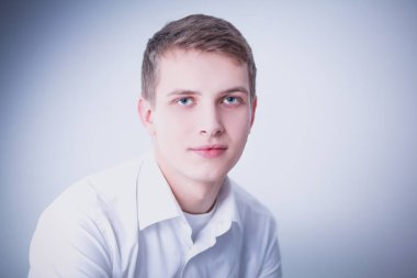 Gri arka plan üzerinde oturan gülümseyen genç adam portresi. Genç adam portresi