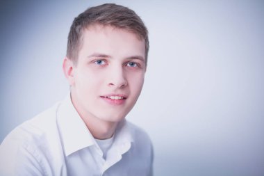 Gri arka plan üzerinde oturan gülümseyen genç adam portresi. Genç adam portresi