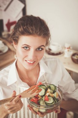 Gülümseyen genç kadın mutfakta salata hazırlık.