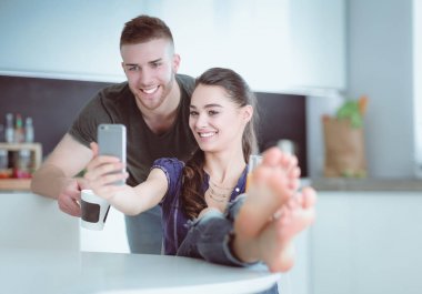 Mutlu çift mutfakta oturmuş smartphone kullanarak