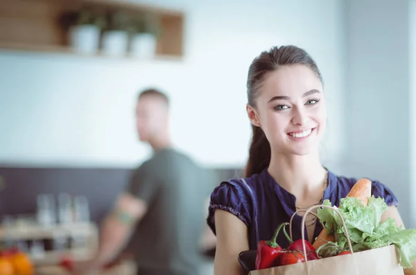 Pareja joven en la cocina, mujer con una bolsa de compras — Foto de Stock