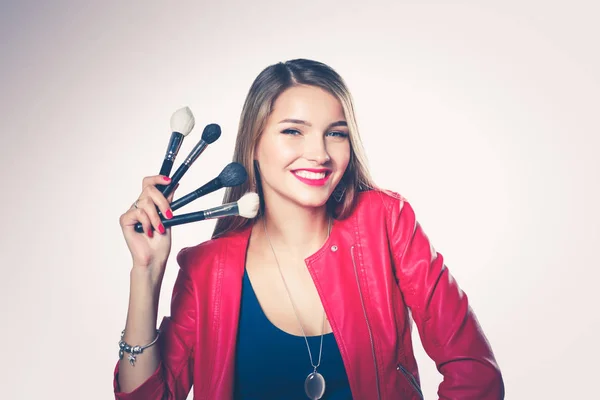 Young beautiful woman holds in one hand and a palette with paint and shadows for makeup, second hand brush for makeup. — Stock Photo, Image