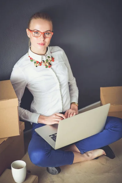 Woman sitting on the floor near a boxes with laptop . Businesswoman