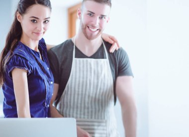 Sebze doğrayan genç bir adam ve mutfakta dizüstü bilgisayarı olan bir kadın.