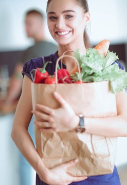 Mutfakta genç bir çift, alışveriş torbası taşıyan bir kadın.