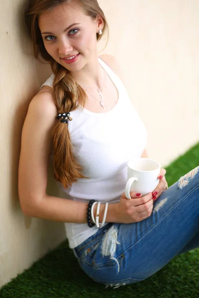 Hermosa mujer sentada en el suelo y sosteniendo una taza. Hermosa mujer —  Fotos de Stock