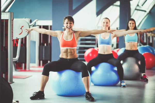 Gente deportiva sentada en colchonetas de ejercicio en un luminoso gimnasio. Chicas deportivas —  Fotos de Stock