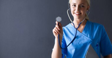 Steteskopla dinleyen kadın doktor, gri arka planda izole edilmiş.