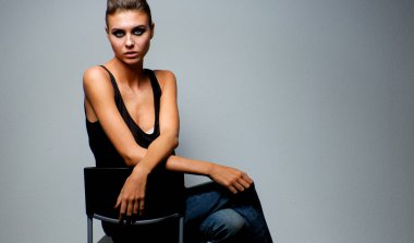 Gri arka plan üzerinde izole bir sandalye oturan güzel kadın