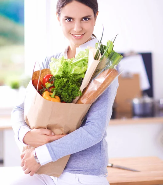 野菜と食料品の買い物袋を持っている若い女性.キッチンに立って — ストック写真