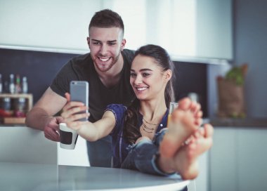 Mutlu çift mutfakta oturmuş smartphone kullanarak
