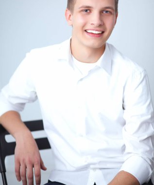 Gri arka plan üzerinde oturan gülümseyen genç adam portresi