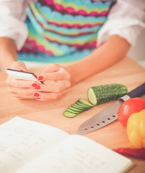 Sorrindo mulher segurando seu celular na cozinha — Fotografia de Stock