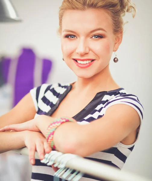 Mooie jonge stylist in de buurt van rack met hangers in office — Stockfoto