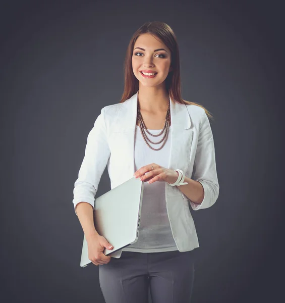 Young woman holding a laptop, standing on gray background — Stock Photo, Image