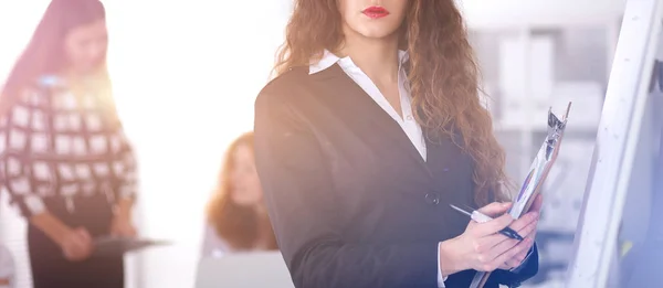 Young woman standing near board with folder — Stock Photo, Image
