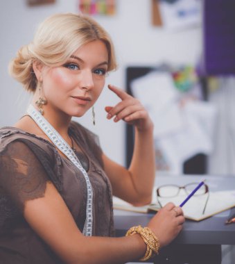 Gülümseyen kadın moda tasarımcısı ofis masasında oturuyor.