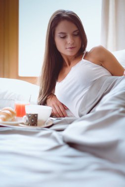 bir bardak süt ile yatakta oturan genç kadın