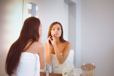 Çekici genç bir kadın yüzüne krem sürüyor.