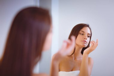 Çekici genç bir kadın yüzüne krem sürüyor.