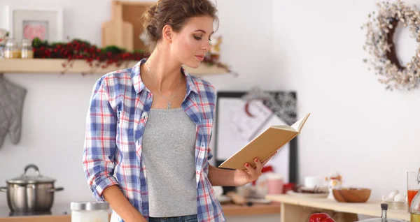 Mujer joven leyendo libro de cocina en la cocina, buscando receta —  Fotos de Stock