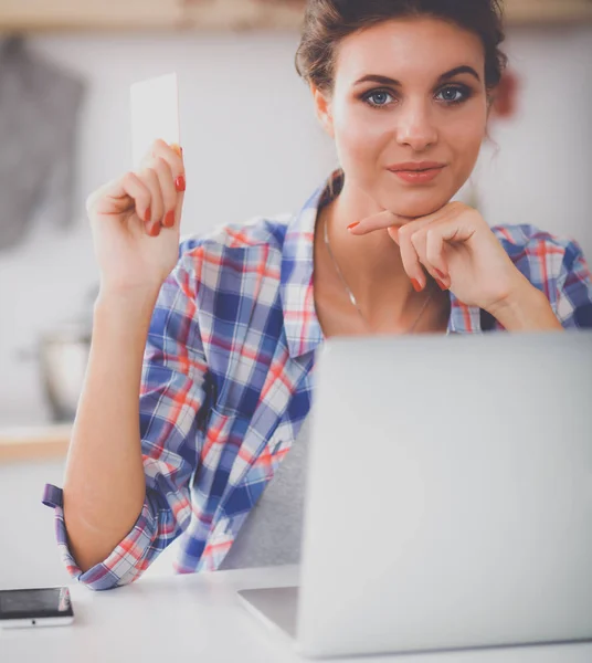 Mosolygós nő online vásárlás számítógéppel és hitelkártyával a konyhában — Stock Fotó