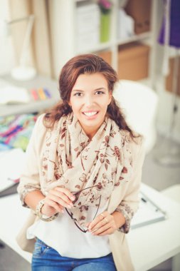 Gülümseyen kadın moda tasarımcısı ofis masasında oturuyor.
