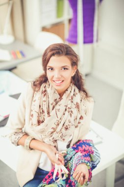 Gülümseyen kadın moda tasarımcısı ofis masasında oturuyor.