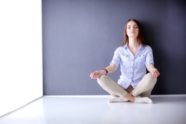 Genç bir kadın yerde, kara duvarın yanında oturuyor.