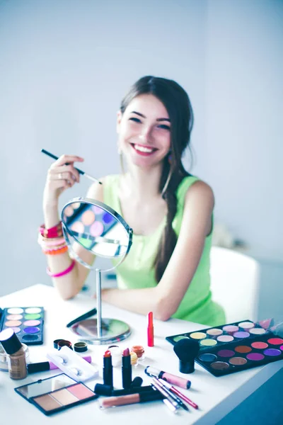 Joven hermosa mujer haciendo maquillaje cerca del espejo, sentado en el escritorio — Foto de Stock