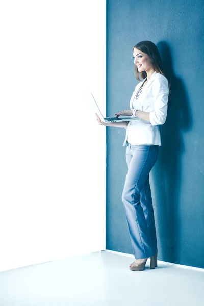 灰色の背景の上に立って、ラップトップを保持している若い女性 — ストック写真