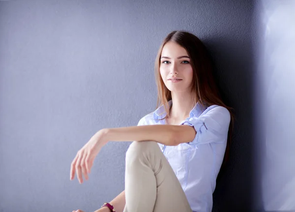 Młoda kobieta siedząca na podłodze przy ciemnej ścianie — Zdjęcie stockowe