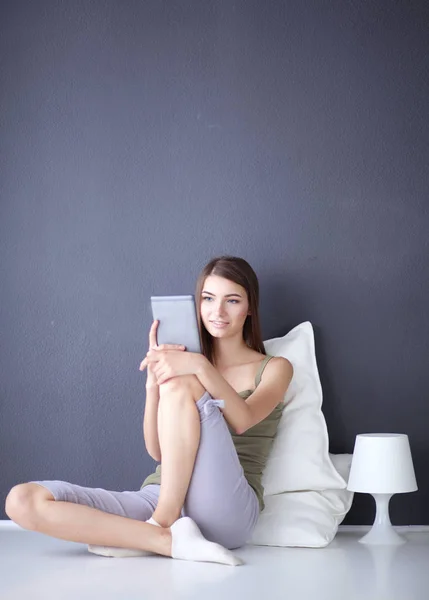 Mulher morena bonita sentada no chão com uma almofada e mesa plana — Fotografia de Stock