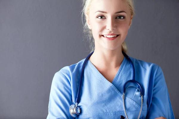 Retrato de médico sonriente en uniforme de pie sobre fondo gris —  Fotos de Stock