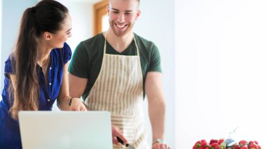 Sebze doğrayan genç bir adam ve mutfakta dizüstü bilgisayarı olan bir kadın.