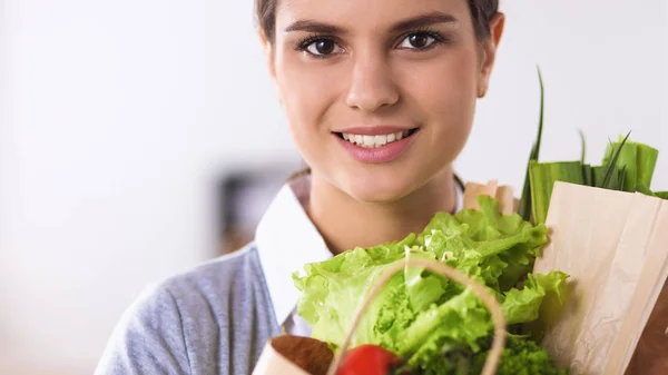 Ung kvinna som håller i matkassen med grönsaker Står i köket. — Stockfoto