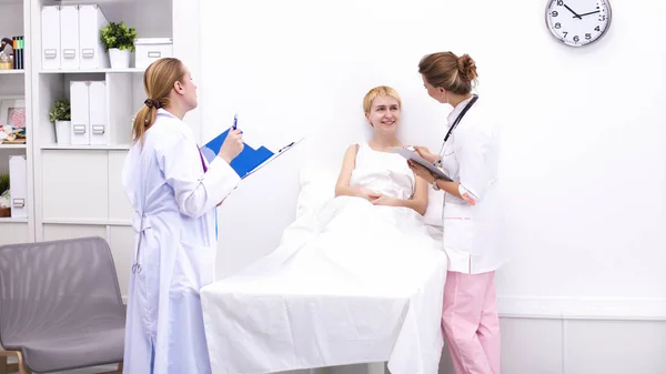 Smiling female doctor with a folder in uniform standing at hospital near patient — Stock Photo, Image