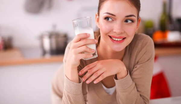 Sonriente joven bebiendo leche, parada en la cocina —  Fotos de Stock