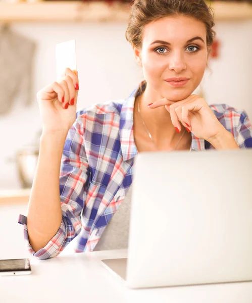Usmívající se žena on-line nakupování pomocí počítače a kreditní karty v kuchyni — Stock fotografie